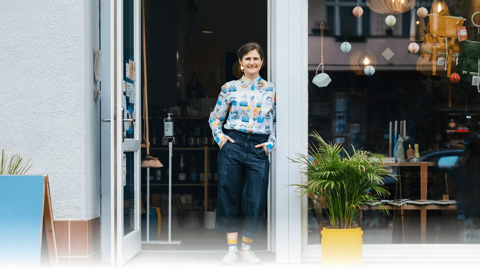 Die Inhaberin eines lokalen Gewerbes steht vor ihrem Laden und lächelt freundlich in die Kamera.